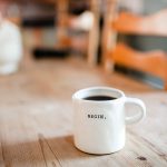 Picture of white coffee cup with the words "Begin" on a table.