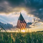 Picture of an American Flag amidst a blue sky and green grass